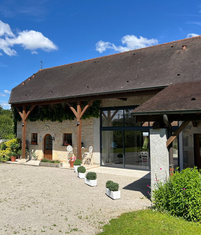 La façade de la grange et sa terrasse meublée, vues depuis la pelouse